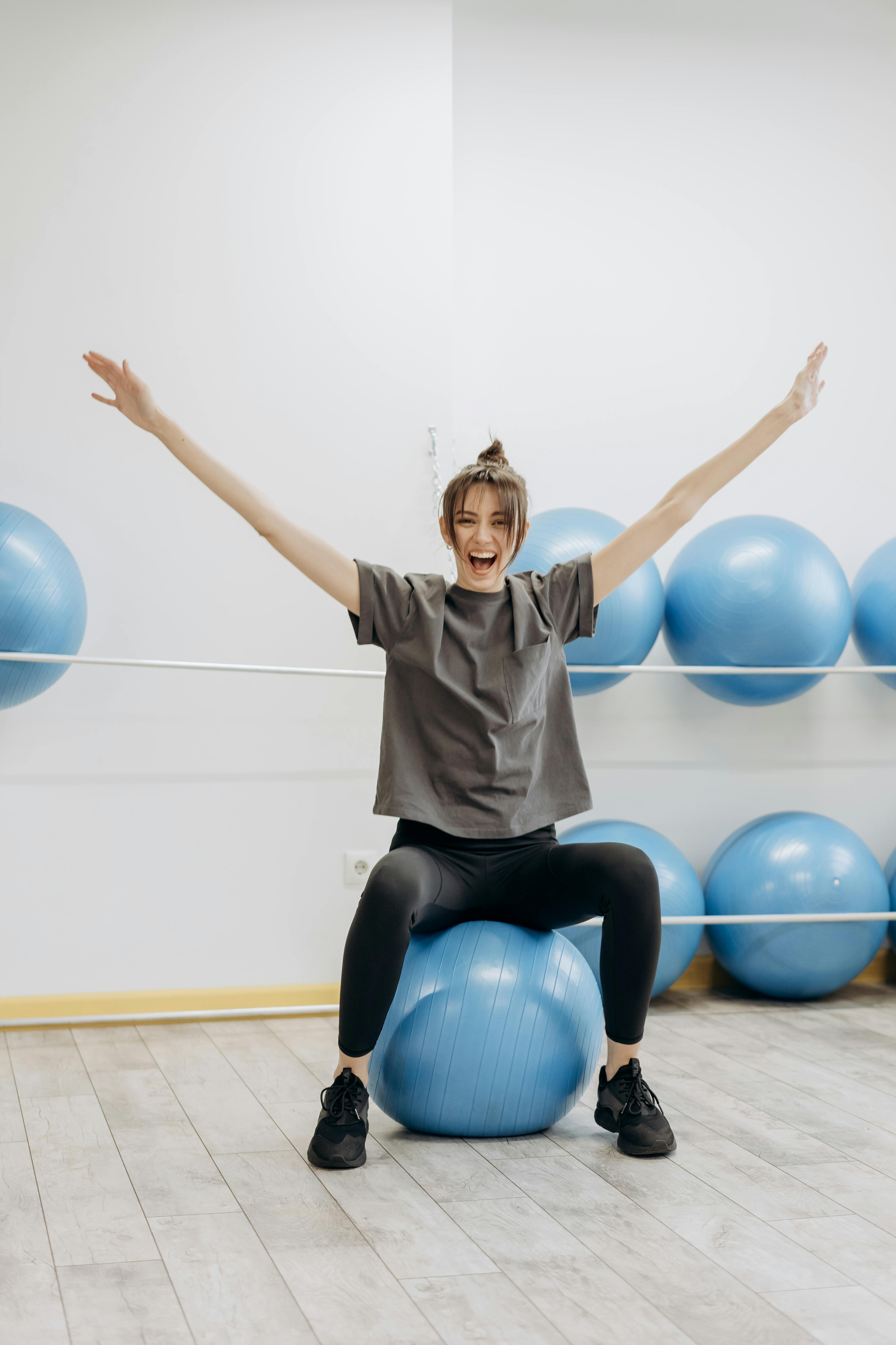happy woman sitting on exercise ball with arms raised